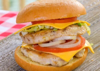 A chicken burger with cheese and tomatoes on a wooden table.