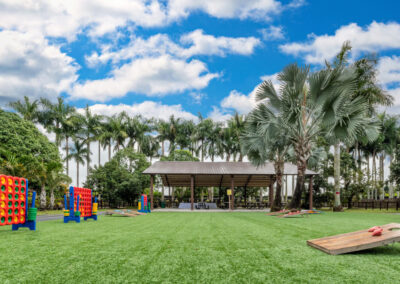 A grassy area with a corn hole game and palm trees.